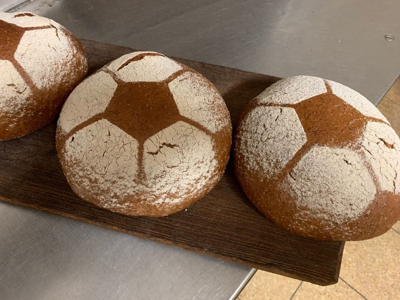 Drei runde Brote mit aufgemehltem Fußball-Muster auf einem Holzbrett